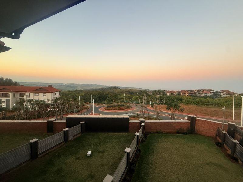Elevated view overlooking a landscaped garden, brick boundary wall, and the surrounding residential estate at sunset.
