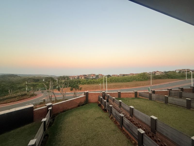Elevated view overlooking a landscaped garden area with brick boundary walls and timber fencing, set against a scenic neighbourhood backdrop.