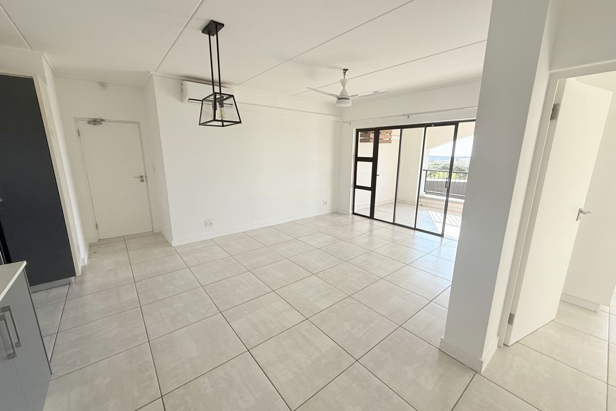 Bright and spacious open-plan living area featuring neutral tiled flooring, a ceiling fan, air conditioning, and direct access to a private balcony.