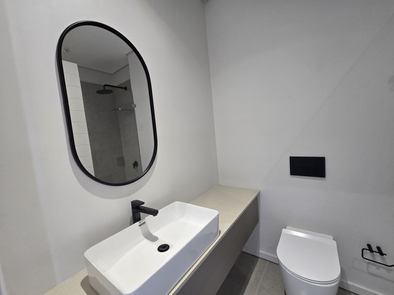 Modern bathroom featuring a wall-mounted vanity with a vessel sink, black fixtures, a wall-hung toilet, and a walk-in shower with a rain shower head.