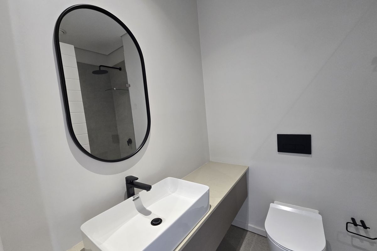 Modern bathroom featuring a wall-mounted vanity with a vessel sink, black fixtures, a wall-hung toilet, and a walk-in shower with a rain shower head.