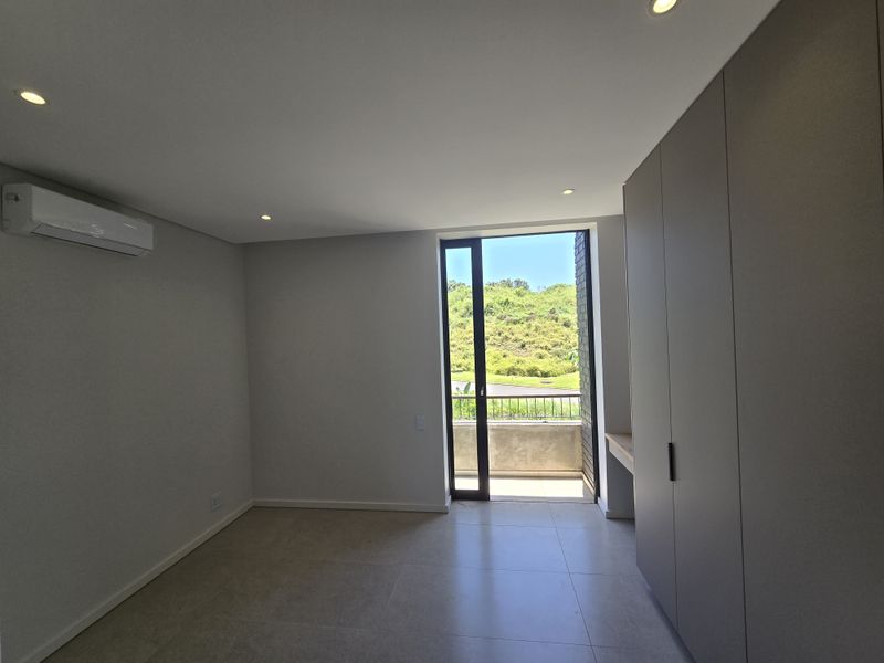 Modern, empty bedroom featuring built-in cupboards, air conditioning, tiled flooring, and direct access to a private balcony with scenic views.