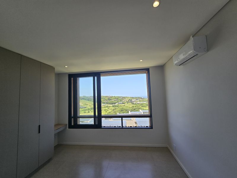 Modern bedroom featuring built-in cupboards, a integrated desk, split-system air conditioning, and large windows offering scenic landscape views.