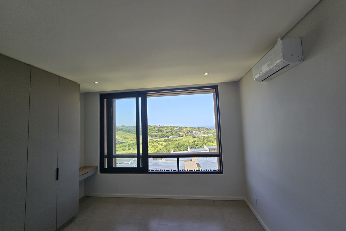 Modern bedroom featuring built-in cupboards, a integrated desk, split-system air conditioning, and large windows offering scenic landscape views.