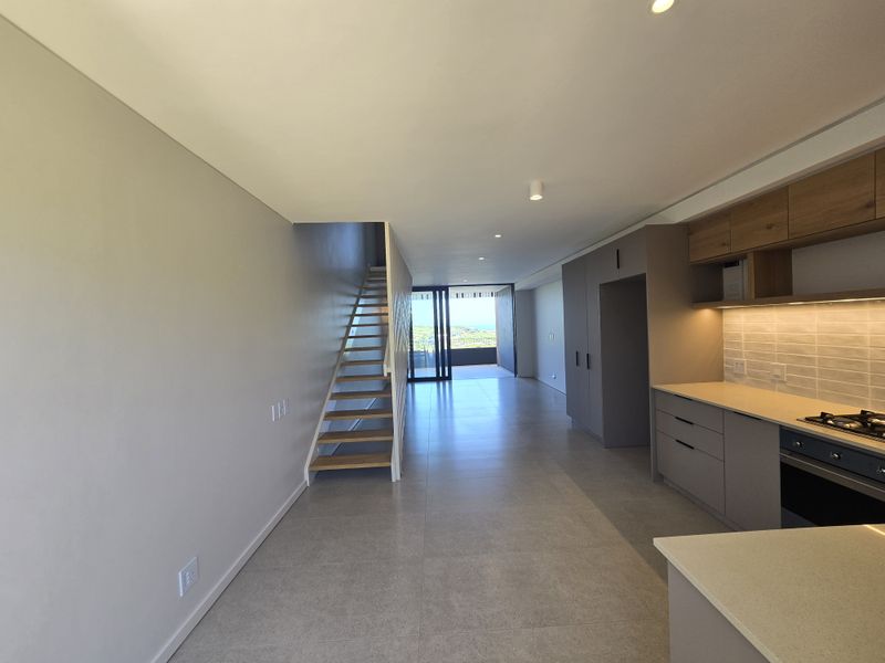 Modern open-plan living area featuring a sleek kitchen with stone countertops, built-in appliances, and a staircase leading to an upper level.