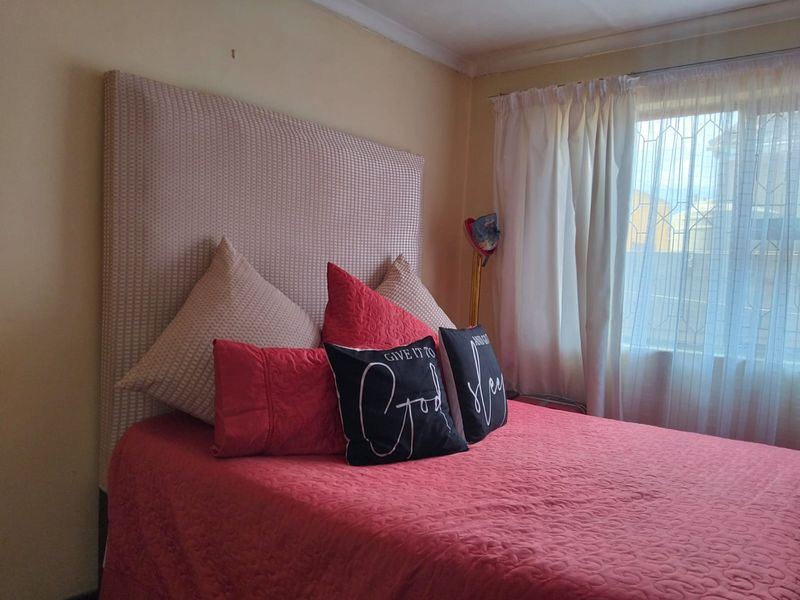 A bedroom featuring a large headboard and a window with curtains, providing natural light to the space.