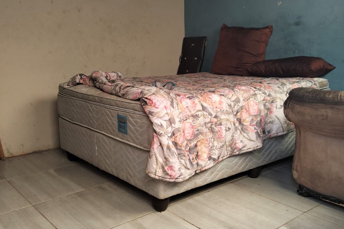 A bedroom featuring tiled flooring and exposed ceiling beams, currently requiring cosmetic updates to the wall finishes.