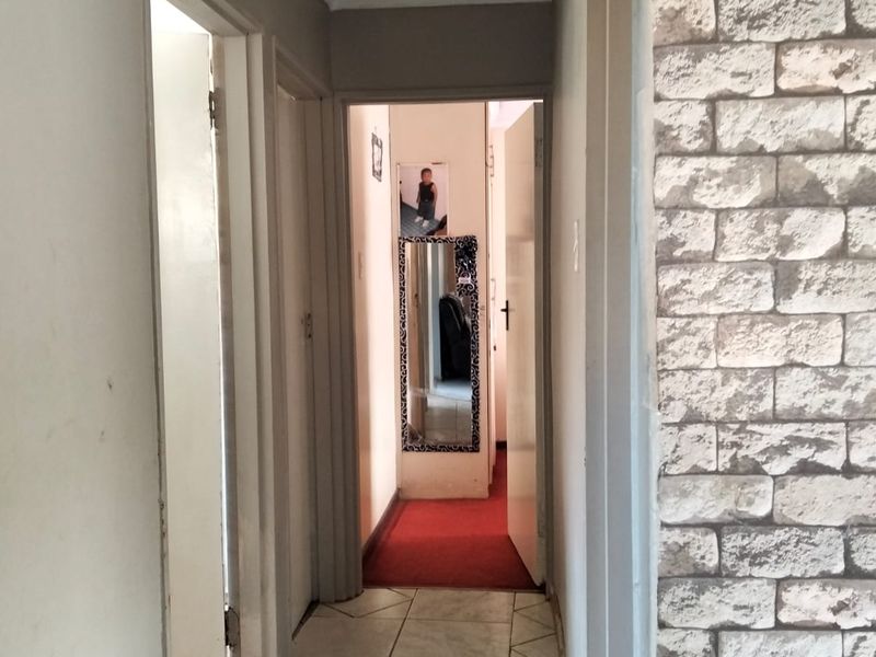 A narrow hallway featuring tiled flooring and a stone veneer accent wall, leading to additional rooms within the home.