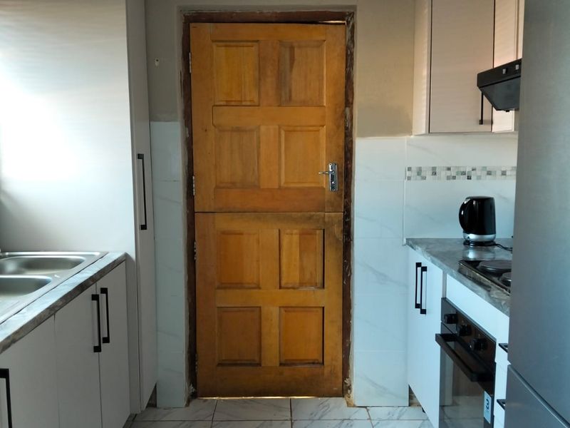 A functional kitchen featuring white cabinetry, marble-look tiled flooring, built-in oven and hob, and a distinctive wooden stable door.