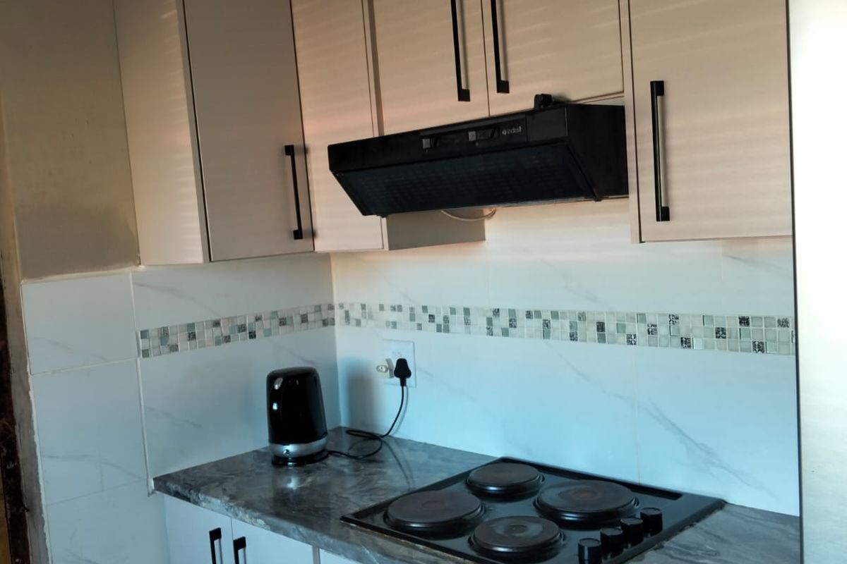 Compact kitchen featuring modern cabinetry, built-in oven, electric hob, extractor fan, and a stylish tiled backsplash with stone-look countertops.