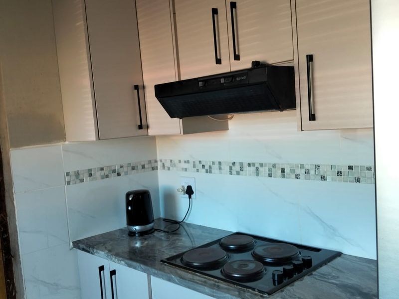 Compact kitchen featuring modern cabinetry, built-in oven, electric hob, extractor fan, and a stylish tiled backsplash with stone-look countertops.