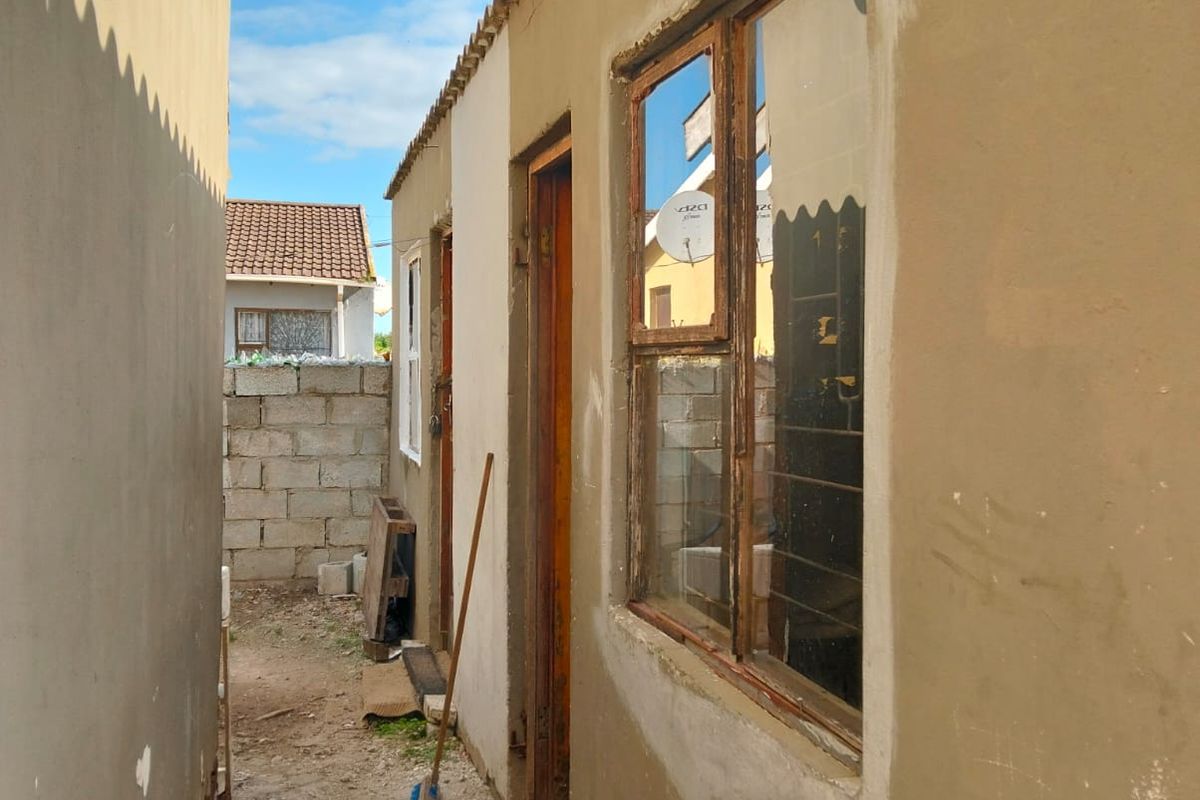 A narrow side passage showing unfinished exterior plastering, timber window frames, and a concrete block boundary wall in a residential setting.