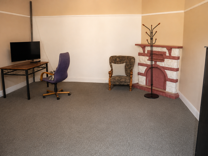 A living room featuring neutral walls, carpet flooring, and a decorative fireplace, offering a versatile space for relaxation or home office use.