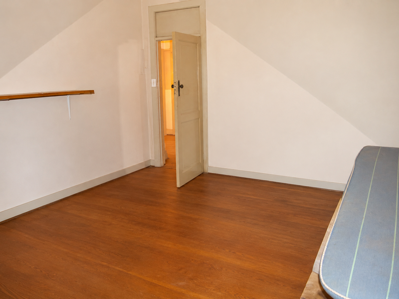 An empty bedroom featuring hardwood flooring, sloped ceilings, and a built-in wall shelf, offering a blank canvas for renovation or staging.