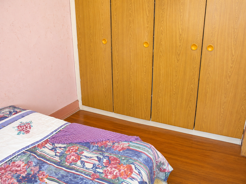 A bedroom featuring built-in wooden wardrobes and laminate flooring, offering a functional storage solution in a dated interior space.