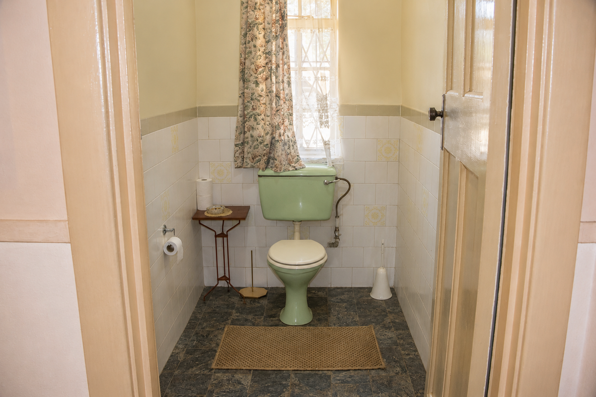 A compact, dated bathroom featuring original green sanitary ware, tiled walls, and vinyl flooring, offering potential for a modern renovation.