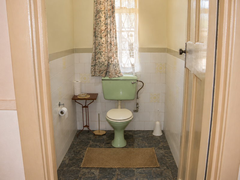 A compact, dated bathroom featuring original green sanitary ware, tiled walls, and vinyl flooring, offering potential for a modern renovation.