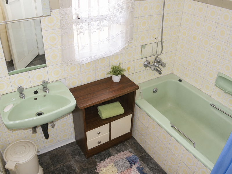 A dated bathroom featuring original green sanitaryware, wall-mounted basin, bathtub with shower mixer, and patterned wall tiling.