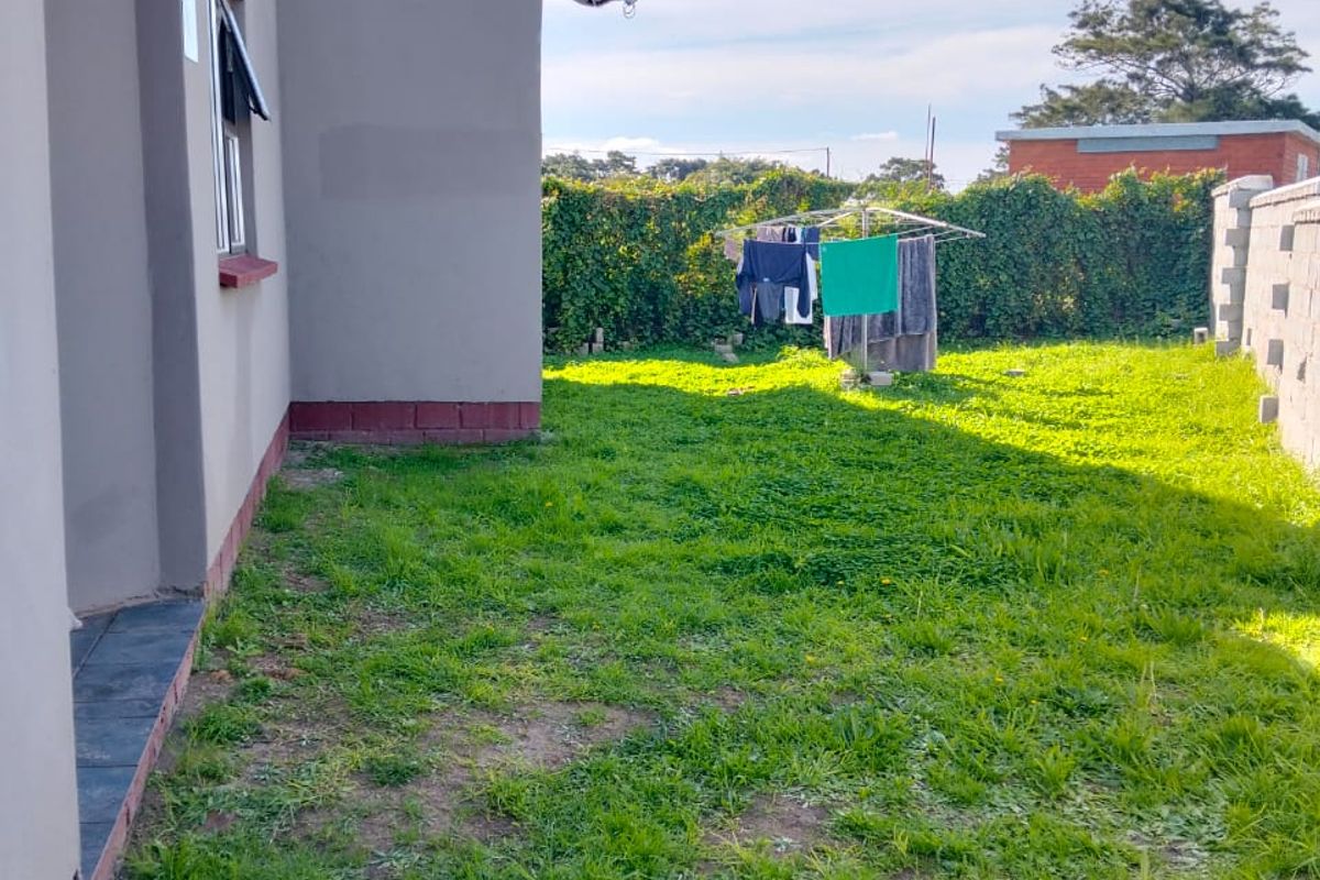 A view of the rear garden area featuring a lawn, boundary wall, and exterior wall of the house with a satellite dish.