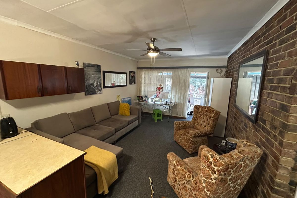 A living room featuring an exposed brick wall, ceiling fan, and wall-mounted cabinetry, with direct access to an outdoor area through a sliding glass door.