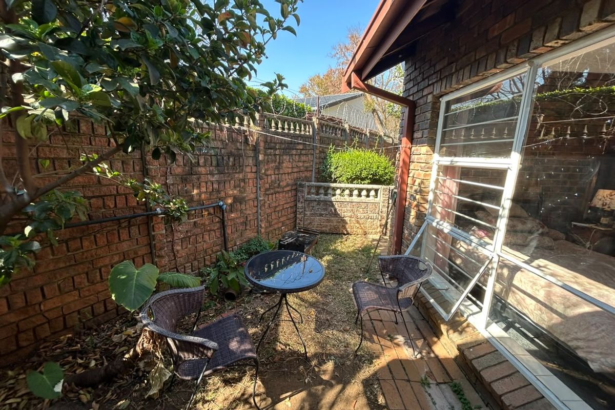 A compact rear courtyard area featuring brick boundary walls, paved sections, and security-barred windows, offering potential for a private outdoor retreat.