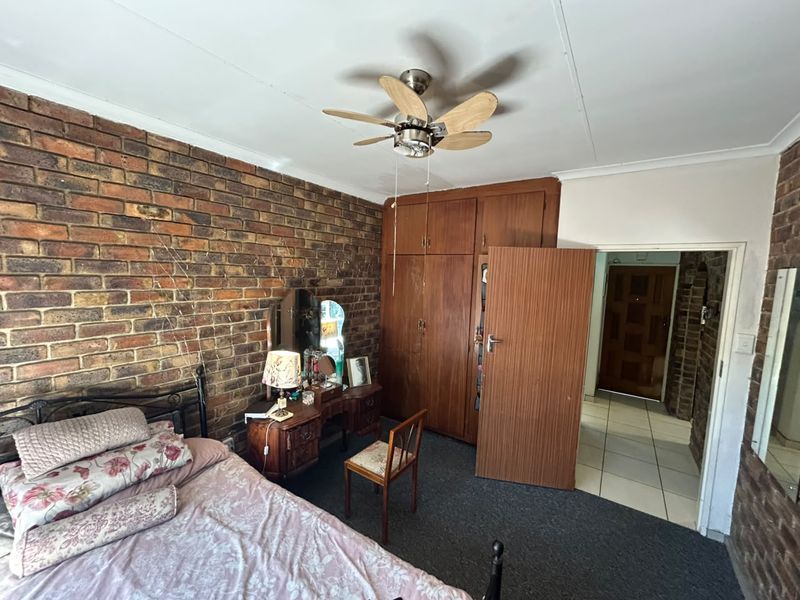 Bedroom featuring an exposed brick feature wall, built-in wooden cabinetry, and a ceiling fan, offering a rustic aesthetic with potential for modernization.