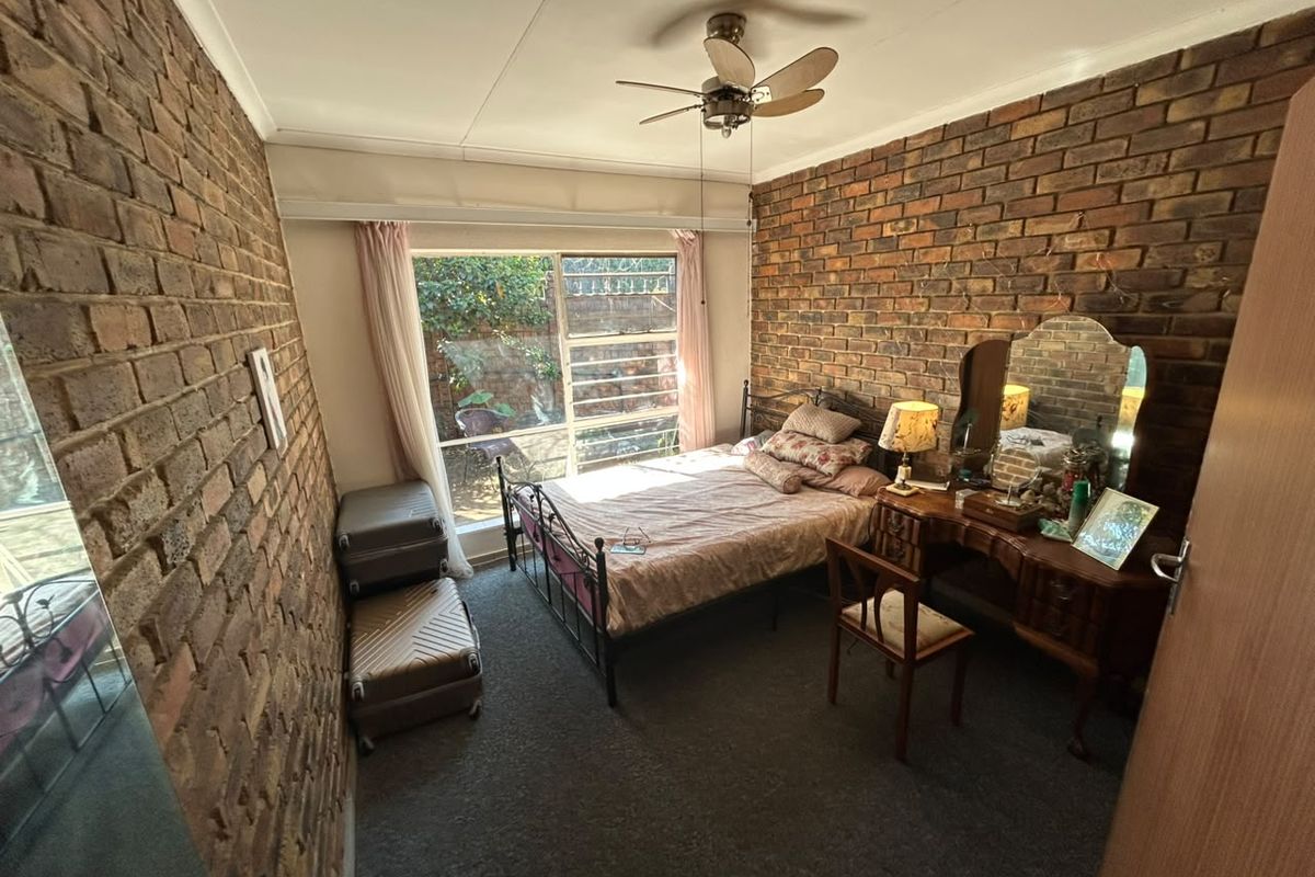 A bedroom featuring exposed brick walls, a ceiling fan, and large windows providing natural light and a view of the garden area.