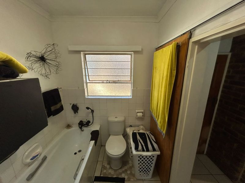 A functional bathroom featuring a bathtub, toilet, and louver window, with a sliding door entrance and tiled splashback areas.