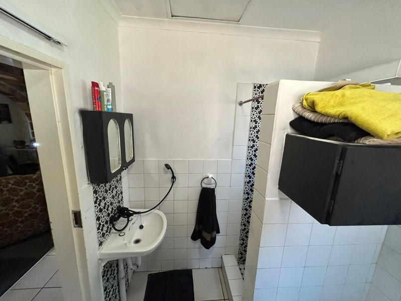 A compact bathroom featuring a wall-mounted basin, tiled splashback, and a shower area with decorative tile accents.