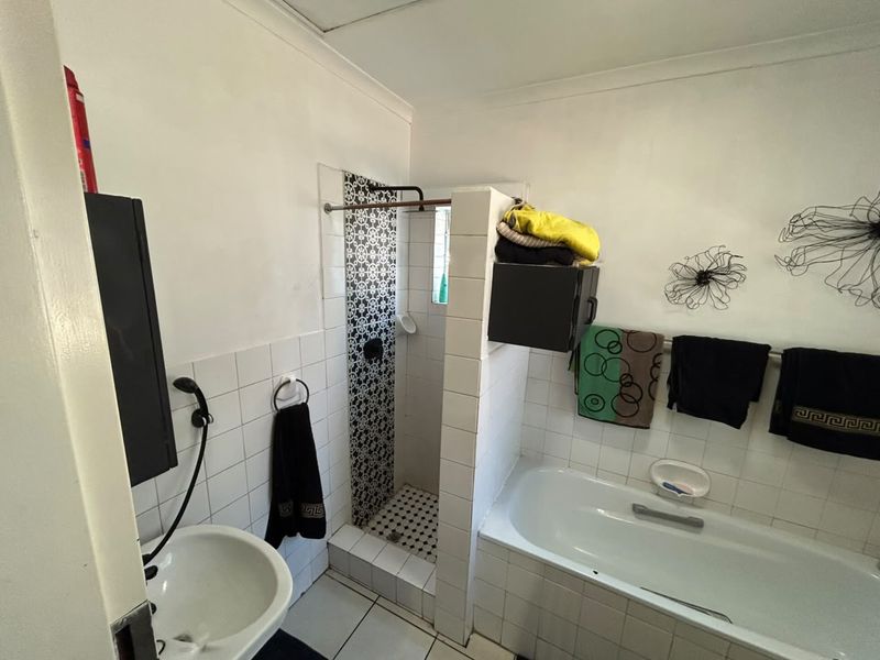 A functional bathroom featuring a built-in bathtub, a separate walk-in shower with decorative tiling, and a pedestal basin.