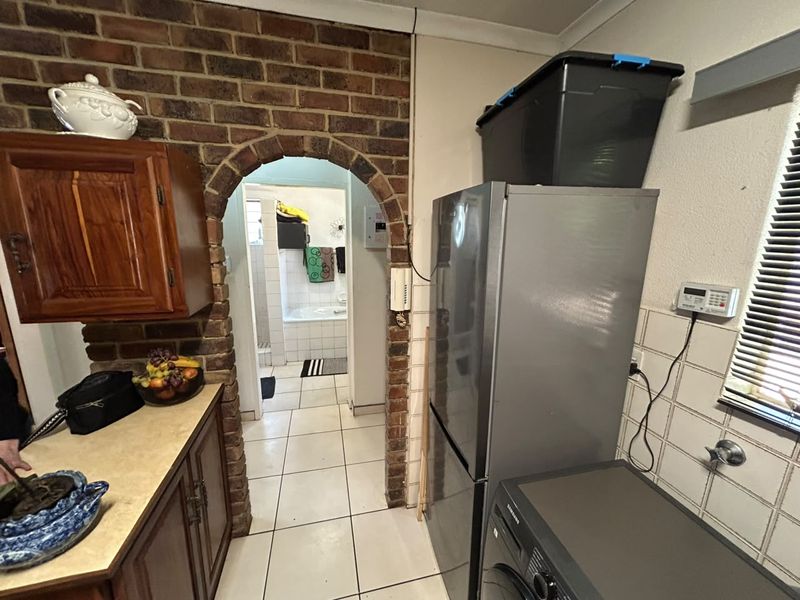 Kitchen area featuring a distinctive brick archway leading to the bathroom, tiled flooring, and traditional wooden cabinetry with laminate countertops.
