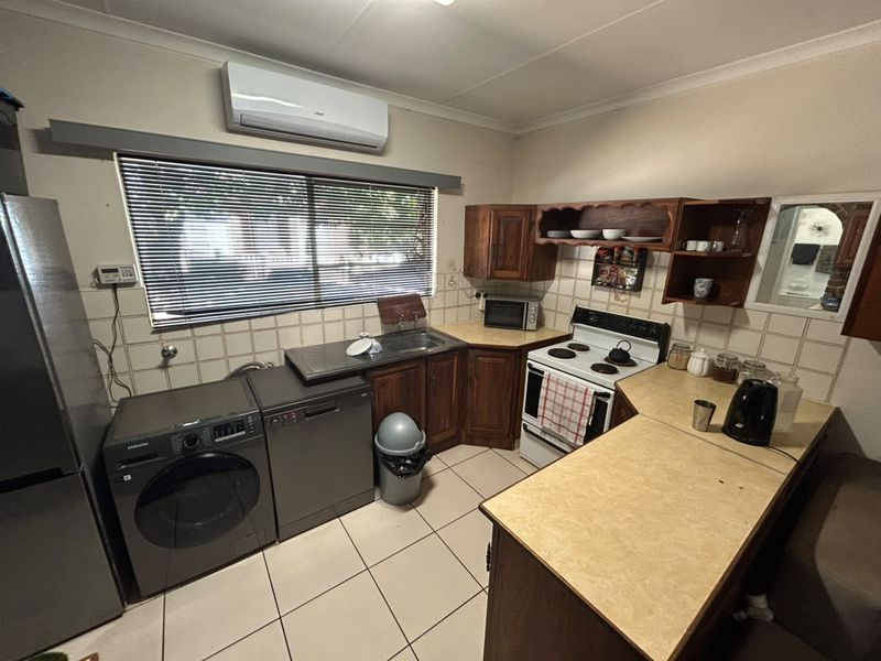 Functional kitchen featuring wooden cabinetry, laminate countertops, tiled backsplash, and integrated space for laundry appliances, offering a practical layout for daily use.