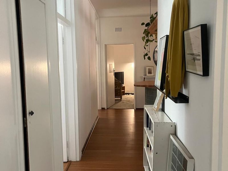 A bright hallway featuring timber flooring and built-in storage cupboards, providing access to the living areas of the apartment.