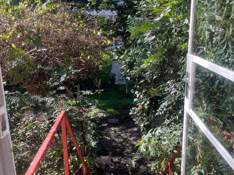 View from a doorway looking out onto a rear garden area via a metal staircase with visible wear and peeling paint.