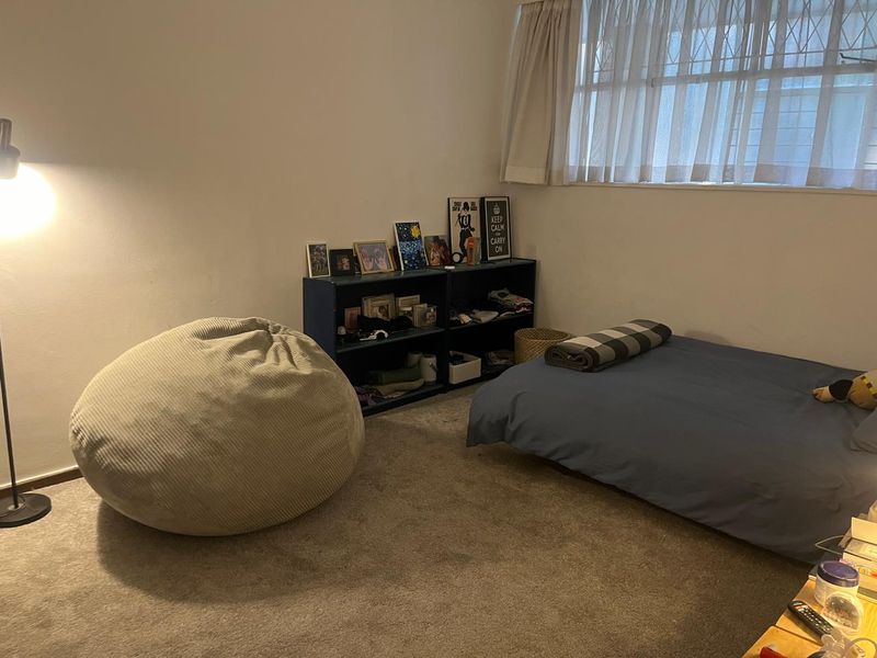 A standard bedroom featuring carpeted flooring, a window with curtain tracks, and an integrated security gate.