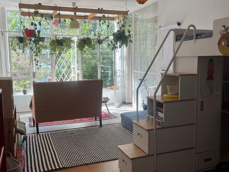 A bright living area featuring large windows that provide ample natural light and a view of the greenery outside, complemented by laminate flooring.