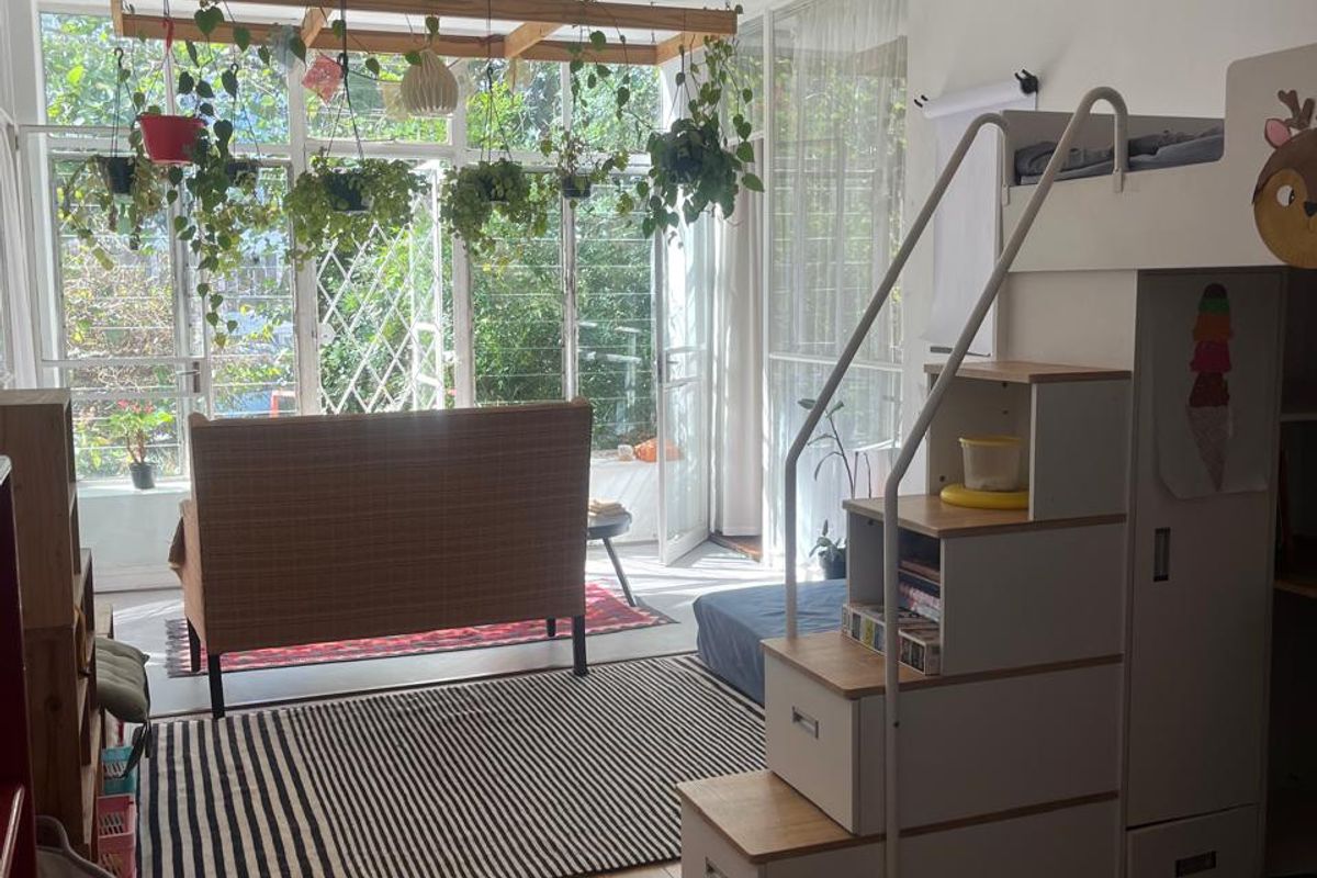 A bright living area featuring large windows that provide ample natural light and a view of the greenery outside, complemented by laminate flooring.