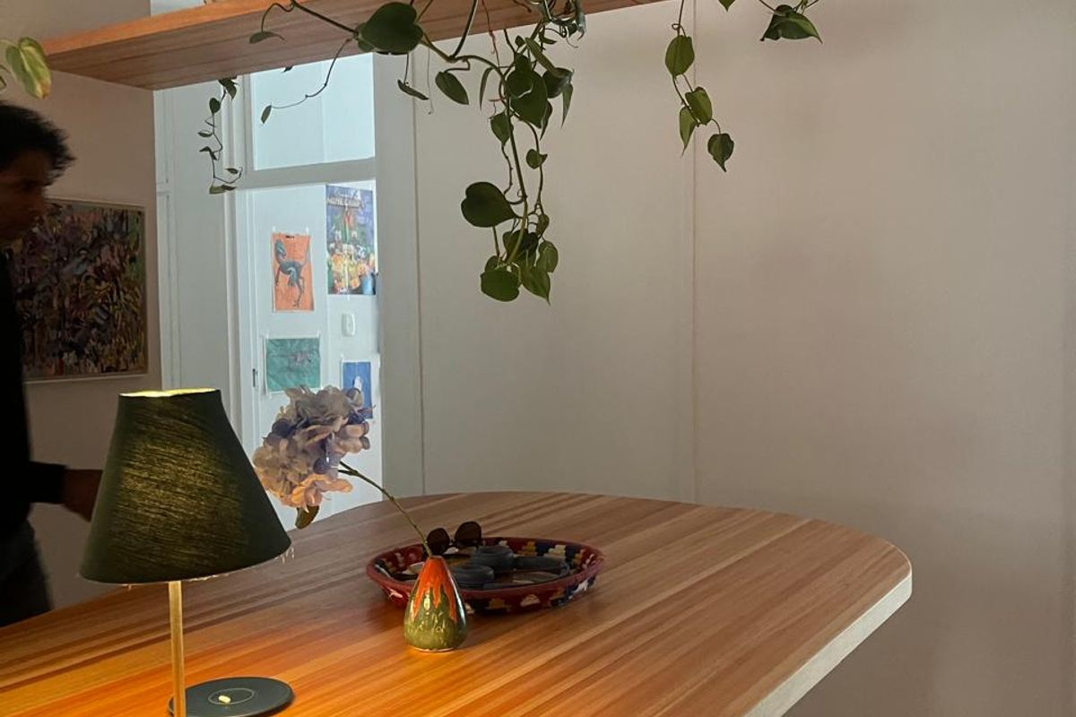 A modern kitchen area featuring a custom wooden breakfast bar with integrated suspended shelving and tiled base detailing.