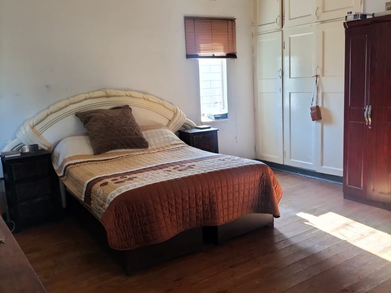 A bedroom featuring original timber flooring, built-in storage cupboards, and a window with a fitted blind.