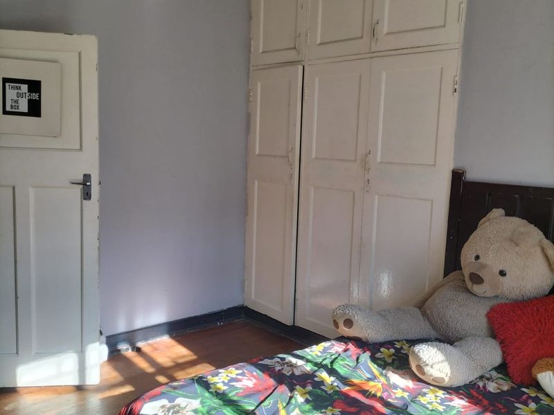 A bedroom featuring built-in cupboards, wooden flooring, and a classic panel door, offering a functional space with potential for cosmetic updates.