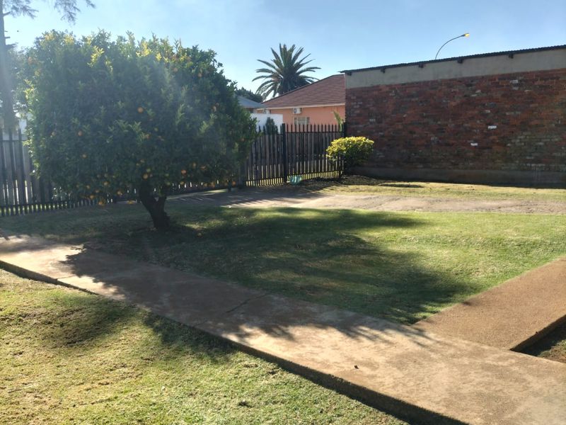 A spacious backyard featuring a lawn, a concrete pathway, and a brick boundary wall with metal perimeter fencing.