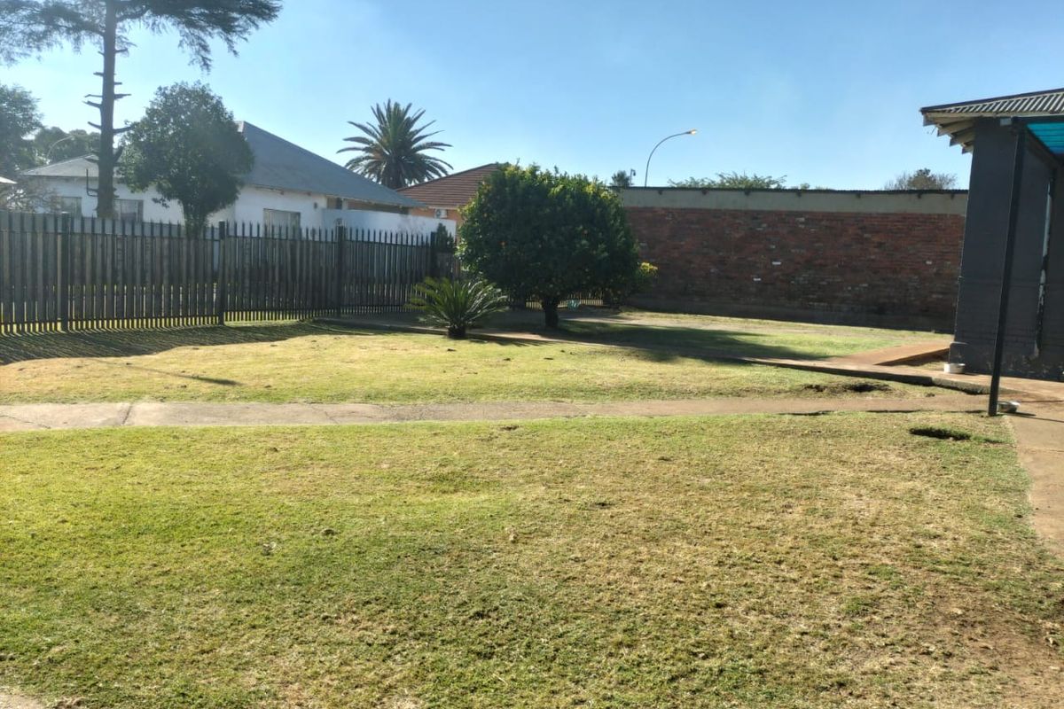A spacious rear garden featuring a lawn, concrete pathways, and secure perimeter fencing with a brick boundary wall.