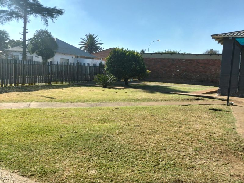 A spacious rear garden featuring a lawn, concrete pathways, and secure perimeter fencing with a brick boundary wall.