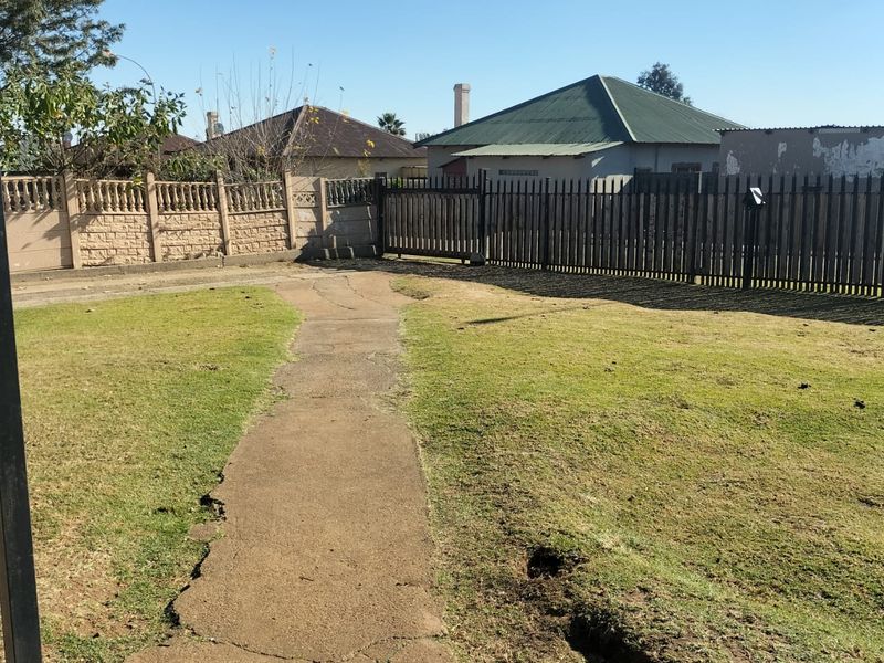 A spacious backyard area featuring a concrete pathway, enclosed by a precast boundary wall and a metal gate.