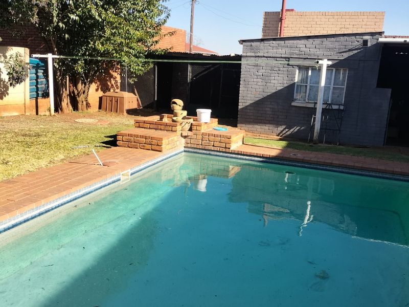 Outdoor pool area featuring a brick-surround swimming pool, a small brick water feature, and an adjacent painted brick outbuilding with a steel window.