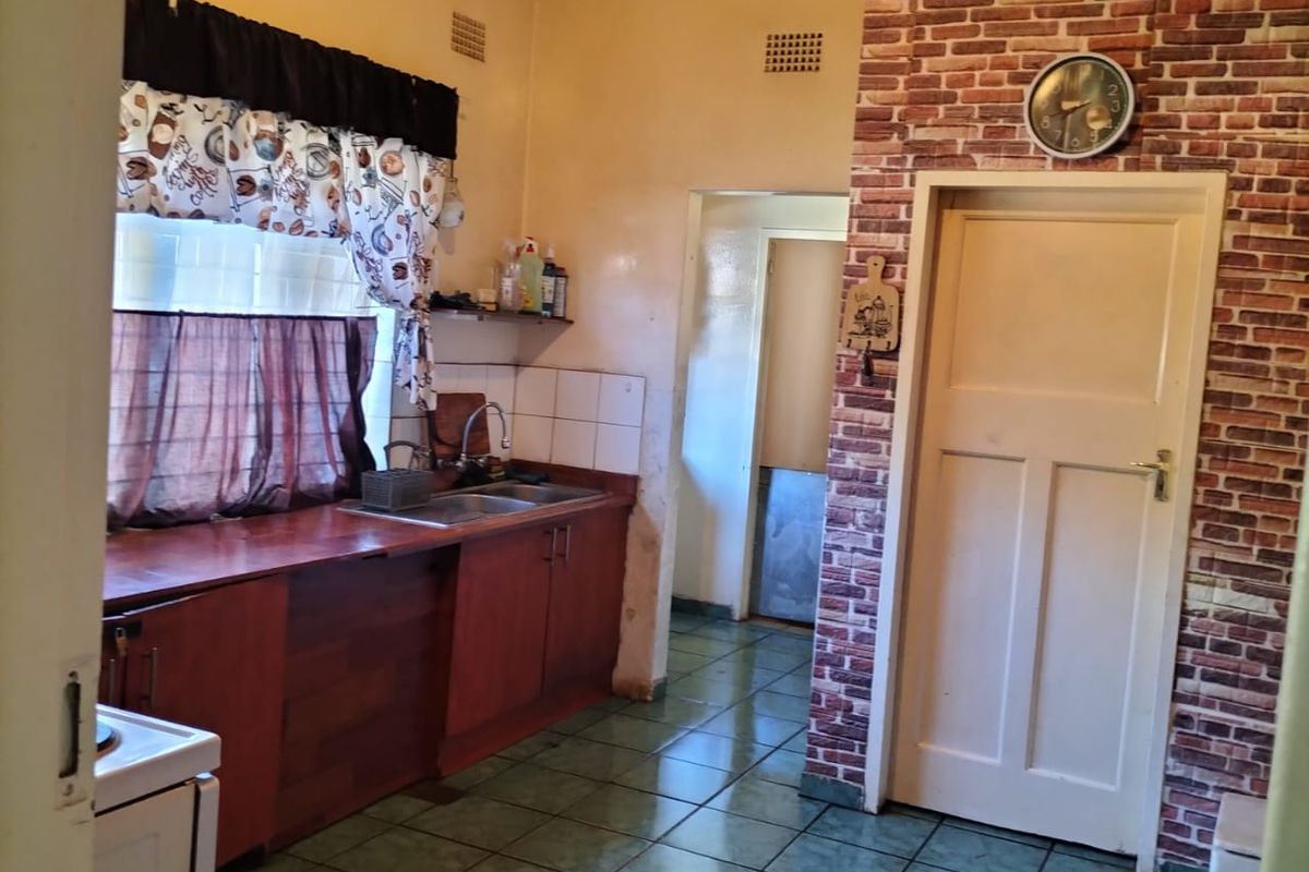 A functional kitchen featuring wooden cabinetry, a stainless steel sink, tiled flooring, and a decorative brick-effect feature wall.