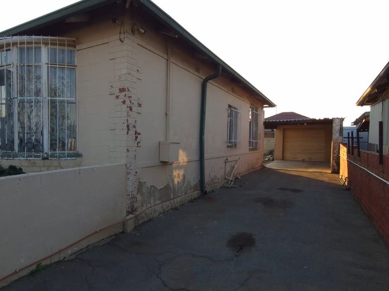 Side view of the property showing a driveway leading to a garage, featuring security bars on windows and visible exterior wall maintenance requirements.