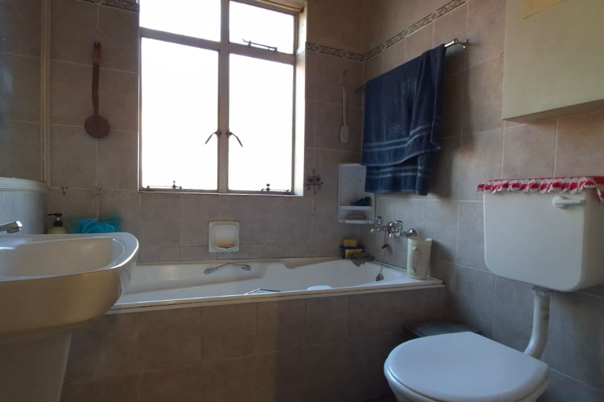 A dated bathroom featuring a pedestal basin, built-in bathtub, and a traditional toilet with a high-level cistern, finished with neutral wall tiles.