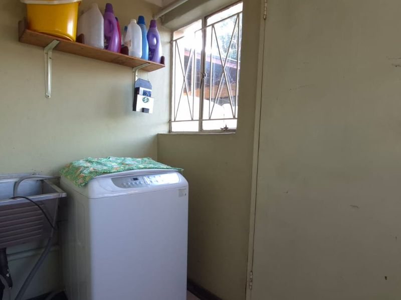 A functional laundry area featuring a stainless steel utility sink, wall-mounted storage shelving, and a window with security bars.