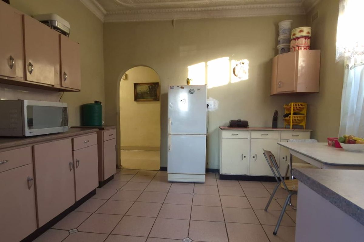 A dated kitchen featuring original cabinetry, tiled flooring, and a classic archway leading to the adjacent living space.